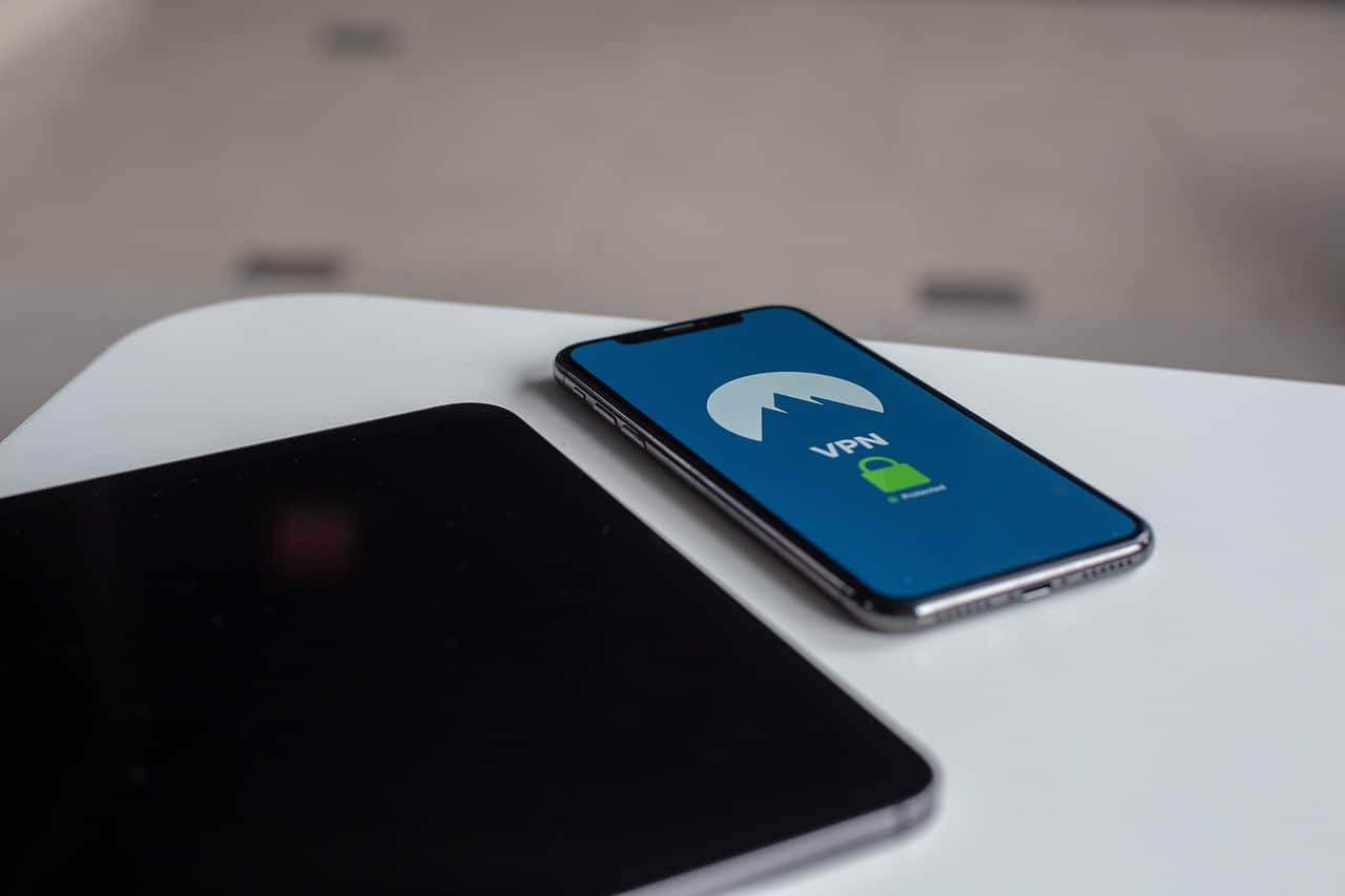Un teléfono móvil sobre una mesa muestra en pantalla una aplicación de VPN con un icono de candado, junto a una tablet apagada, representando seguridad y protección de la conexión digital.
